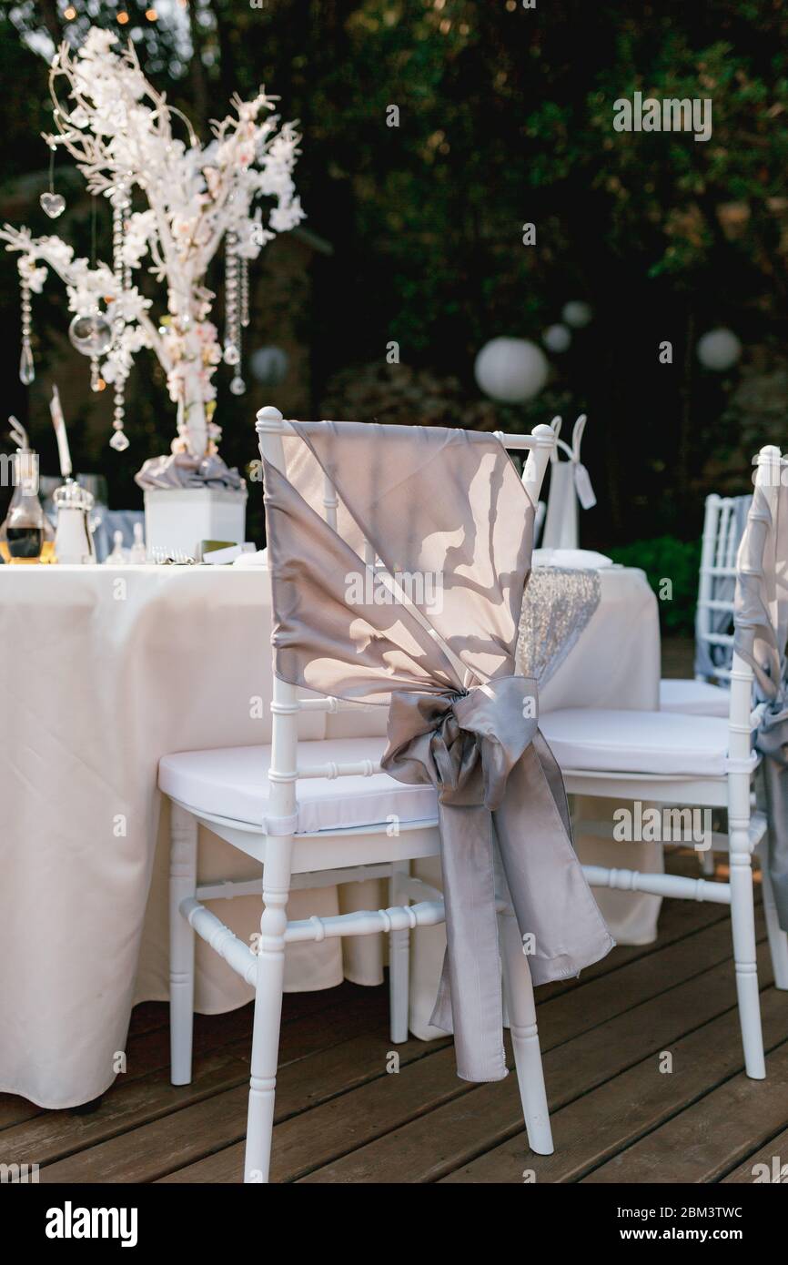 Tavoli rotondi con tovaglia in tessuto bianco, sedie bianche Chiavari con  tessuto grigio drappeggio con arco. Al centro del tavolo c'è il cristallo  Foto stock - Alamy