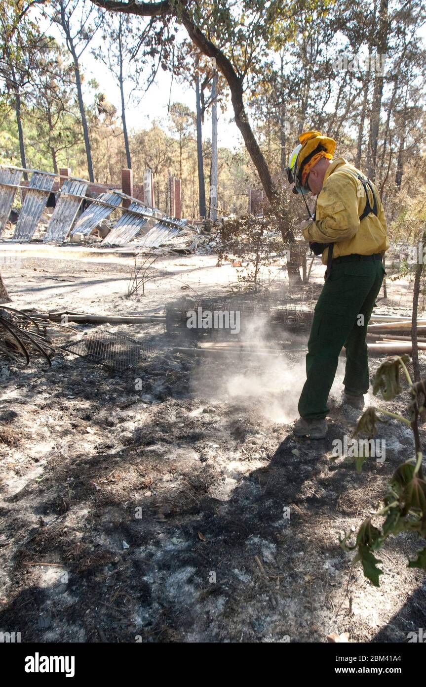 Bastrop County Texas USA, 9 settembre 2011: I vigili del fuoco indossano un elmetto alla ricerca di punti caldi di fronte all'edificio in metallo collassato in un quartiere rurale vicino a Bastrop. L'area boschiva è stata colpita duramente quando un incendio della foresta si è abbattuto sui boschi di piney appena giorni prima. ©Marjorie Kamys Cotera/Daemmrich Photography Foto Stock