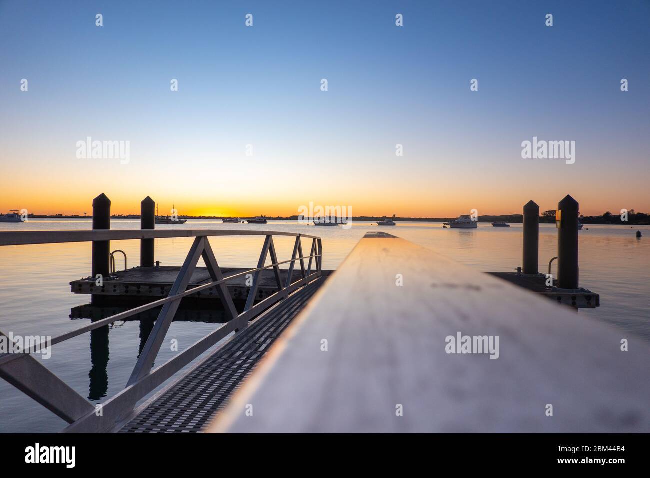 Molo che proietta nel porto di Tauranga all'alba con le linee di guida della ringhiera pedonale. Foto Stock