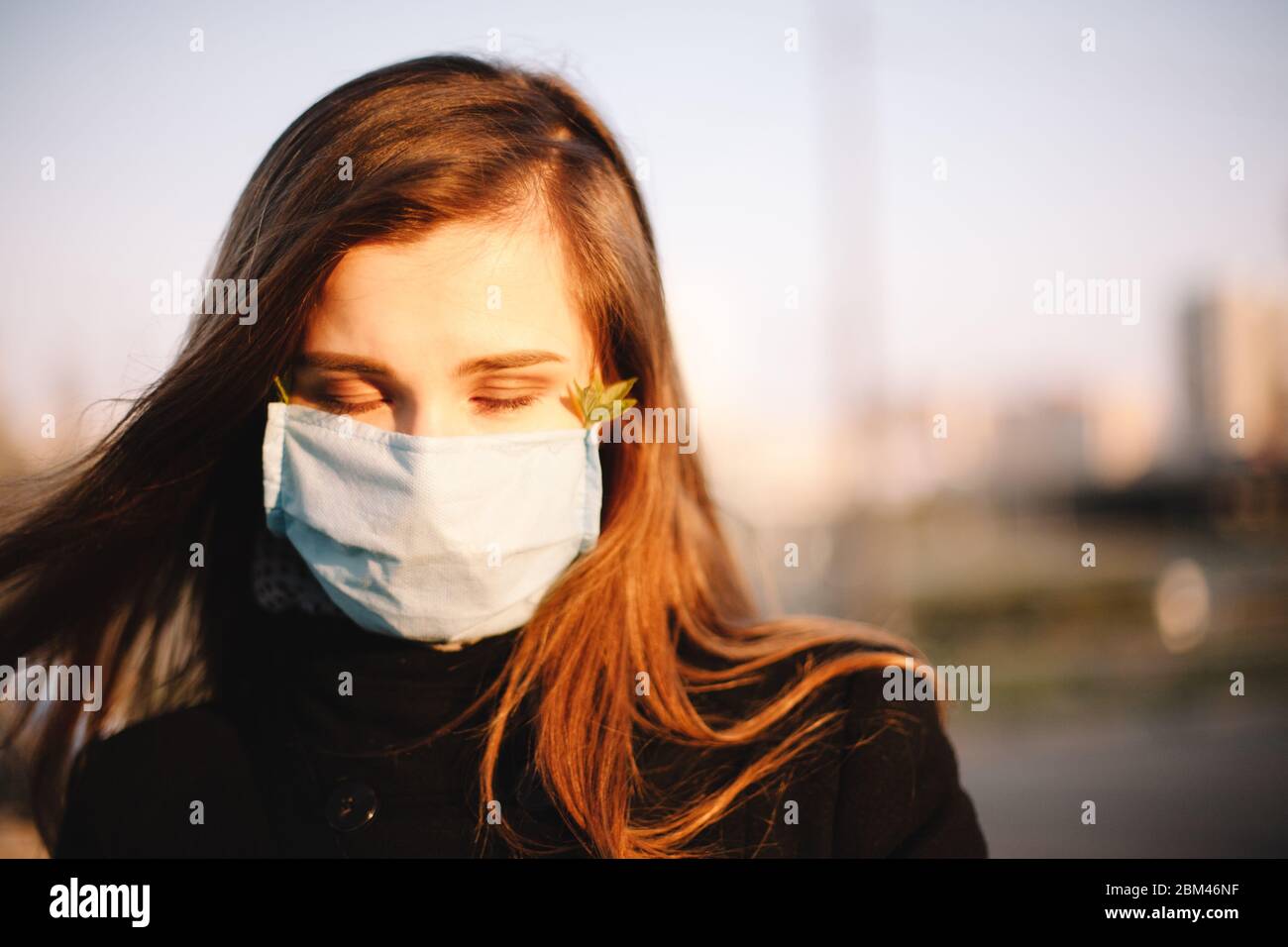 Primo piano ritratto di ragazza triste adolescente che indossa maschera medica viso protettivo in piedi all'aperto sulla strada della città Foto Stock