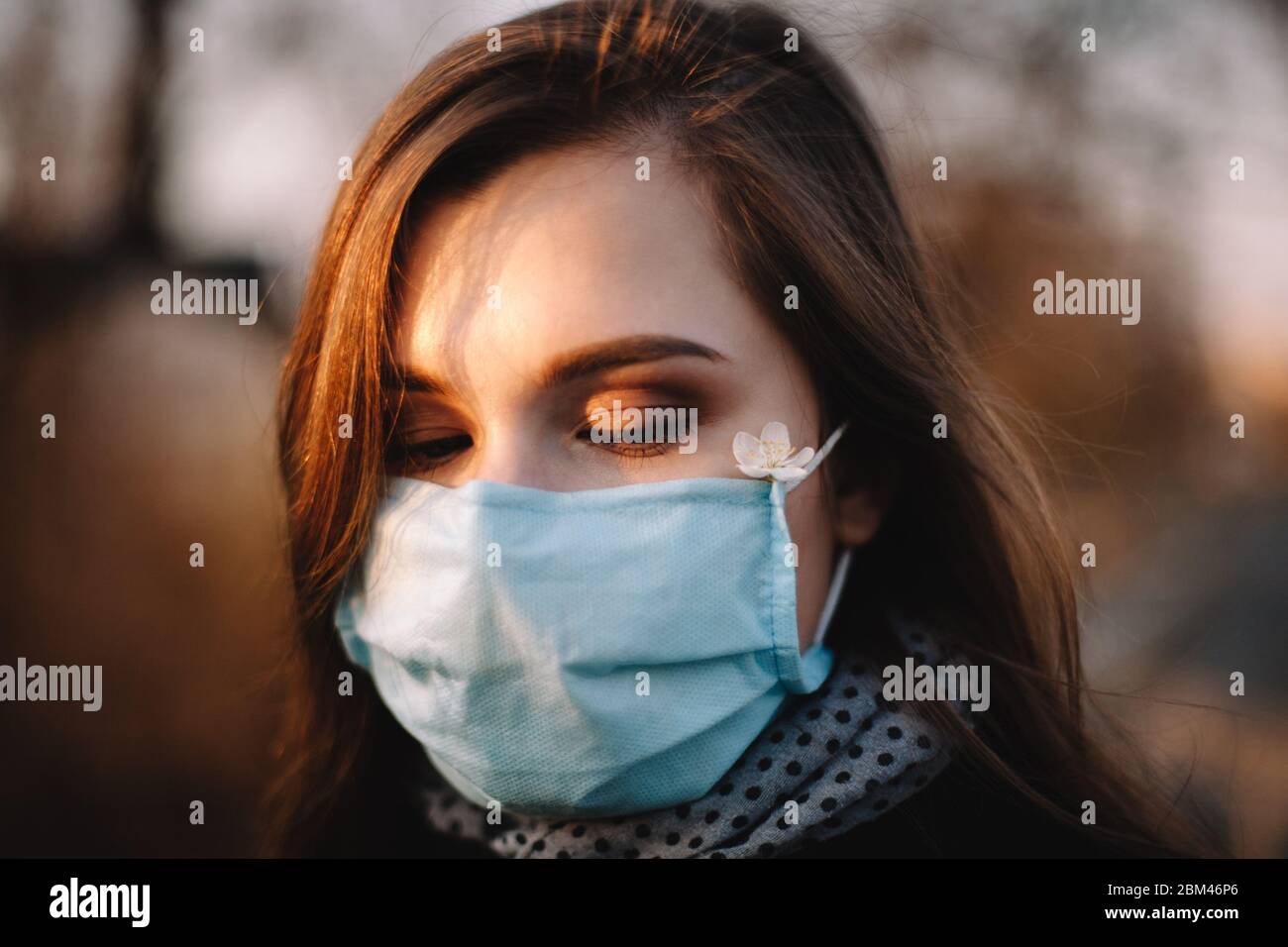 Primo piano ritratto di ragazza triste adolescente indossare maschera medica viso protettivo in piedi all'aperto nel parco durante la primavera Foto Stock