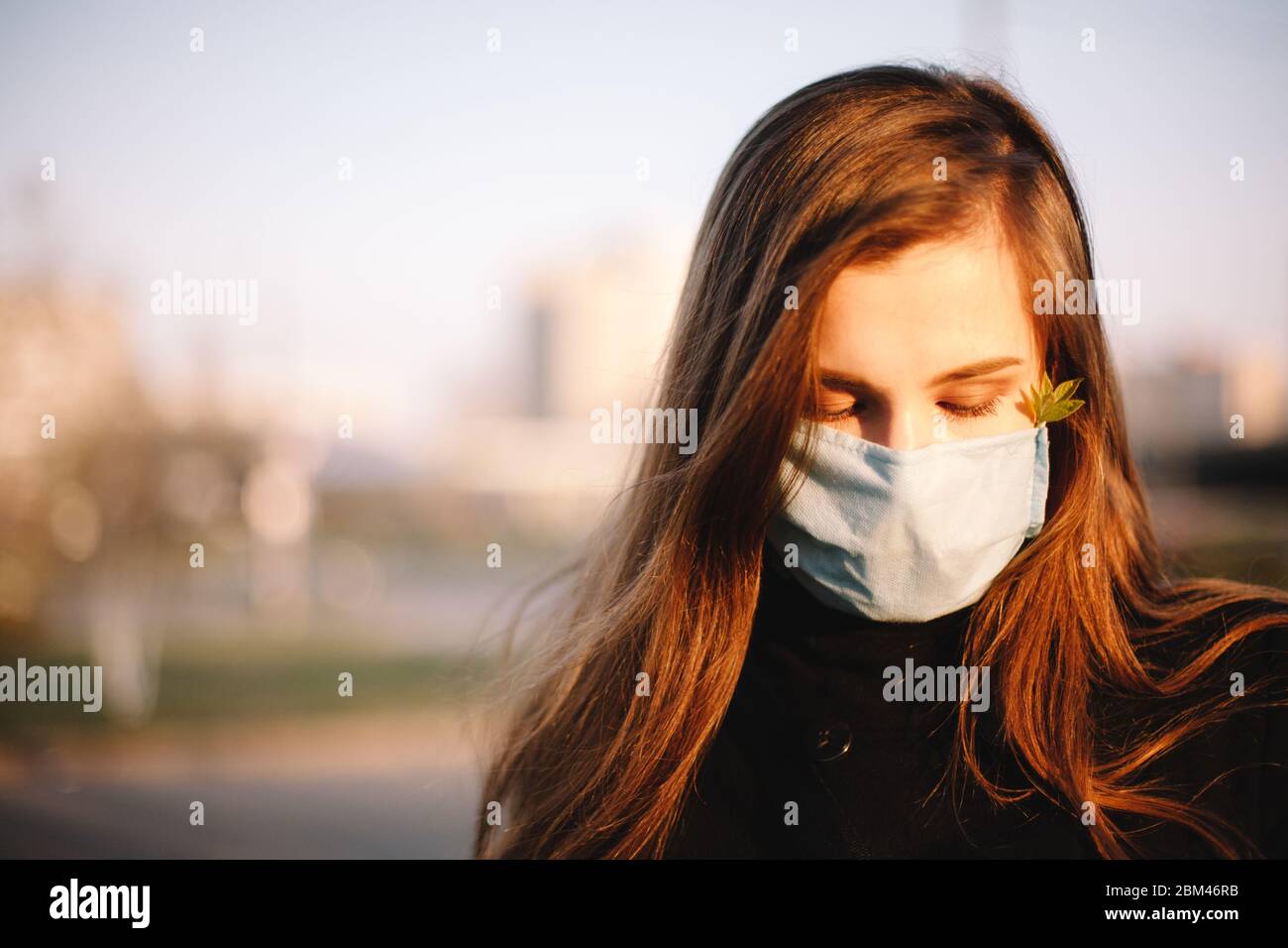 Ritratto di ragazza adolescente triste che indossa maschera medica facciale protettiva in piedi all'aperto sulla strada della città Foto Stock