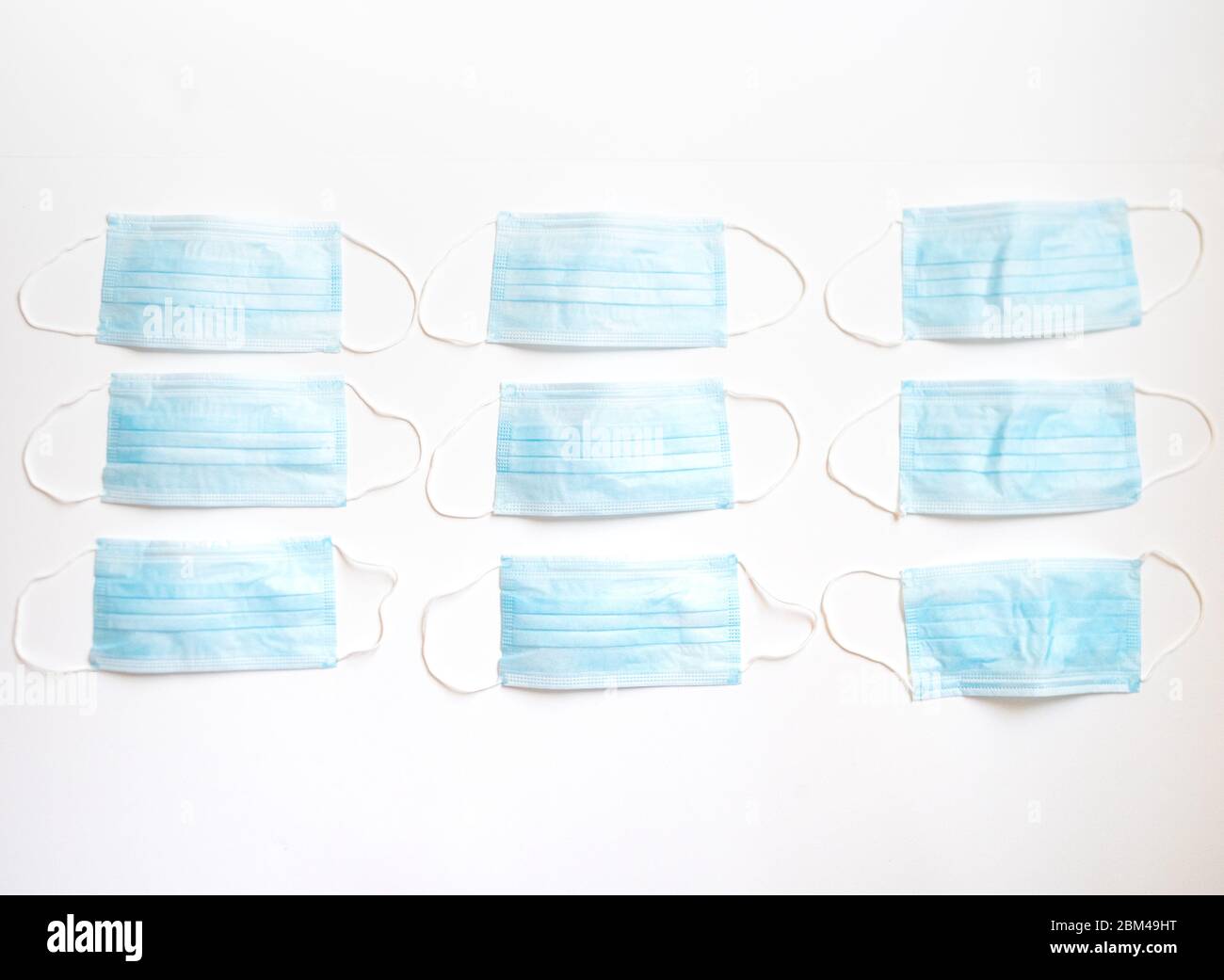 File di maschere facciali monouso di colore azzurro con fasce elastiche su sfondo bianco. Profondità di campo bassa. Foto Stock