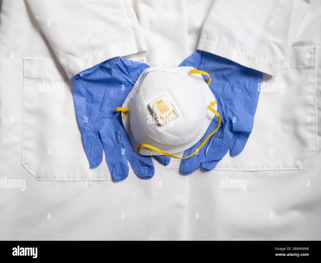 Cappotto medico bianco, un paio di guanti monouso blu e una maschera facciale 3M N-95. Foto Stock