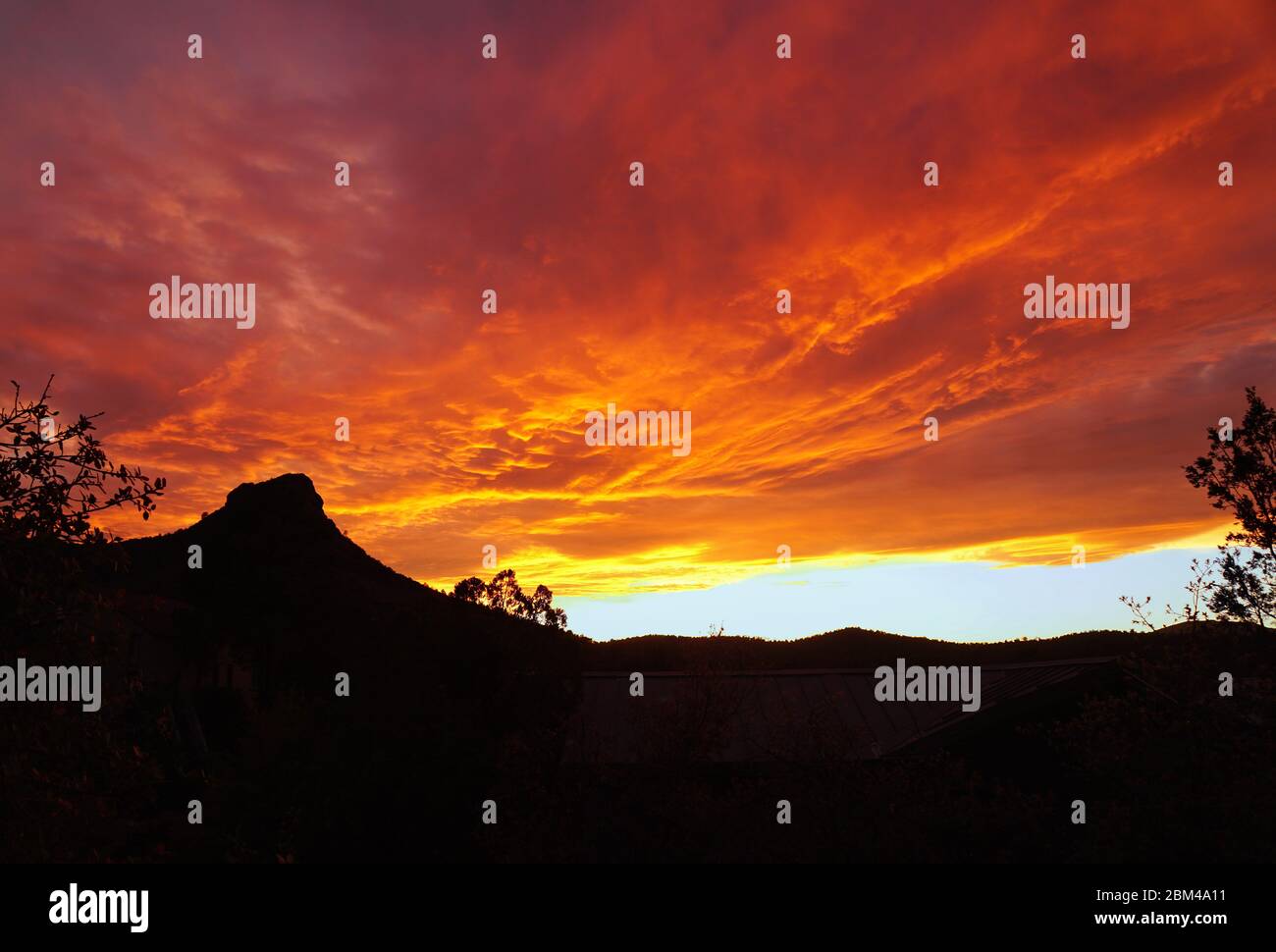 Un tramonto ardente crea colori drammatici sulla silhouette di Thumb Butte. Foto Stock