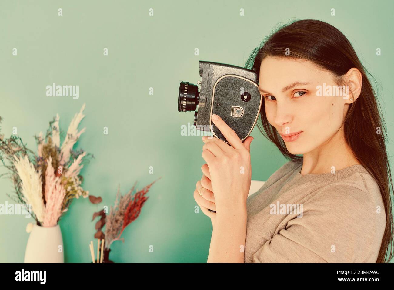 bella ragazza in jeans blu con una fotocamera retro in mano su uno sfondo turchese, guardare la fotocamera Foto Stock