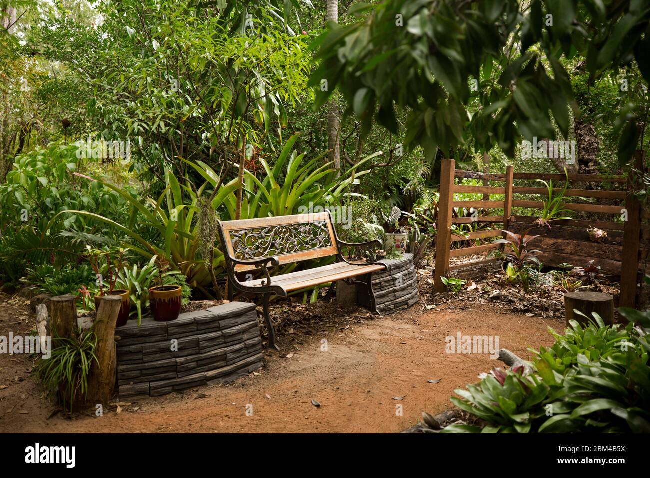 Bancale decorativo in legno e ferro battuto con pareti adiacenti in pietra circondate da alberi e fitta vegetazione in giardino sub-tropicale in Australia Foto Stock
