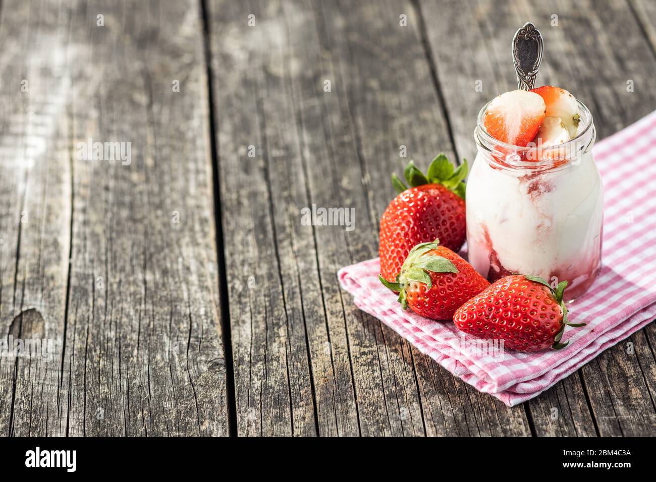 Yogurt bianco fruttato in vaso e fragole su tavolo di legno. Foto Stock