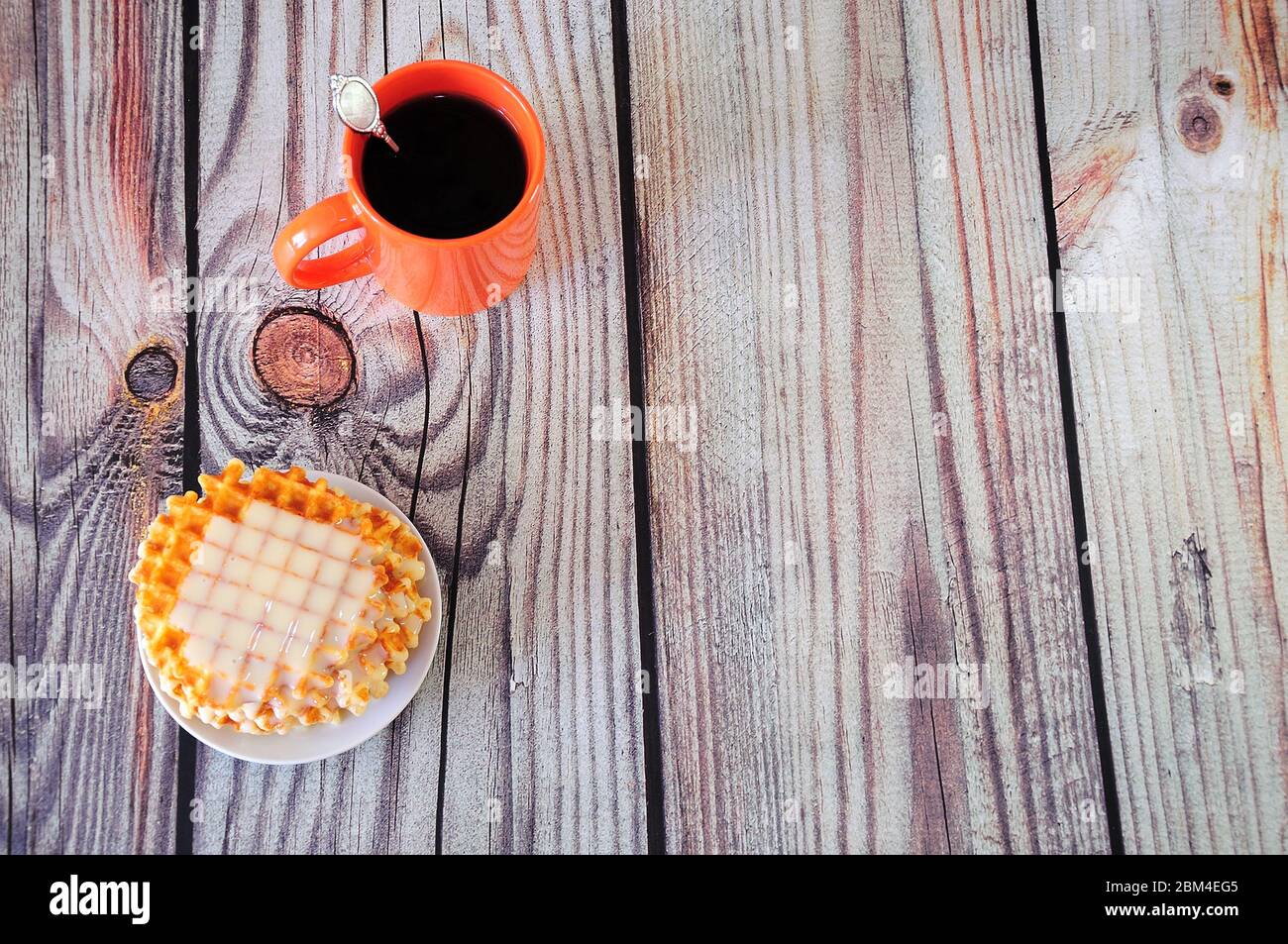 Una tazza di caffè caldo in ceramica arancione e un piatto con waffle parigini e sciroppo cremoso. Primo piano. Foto Stock