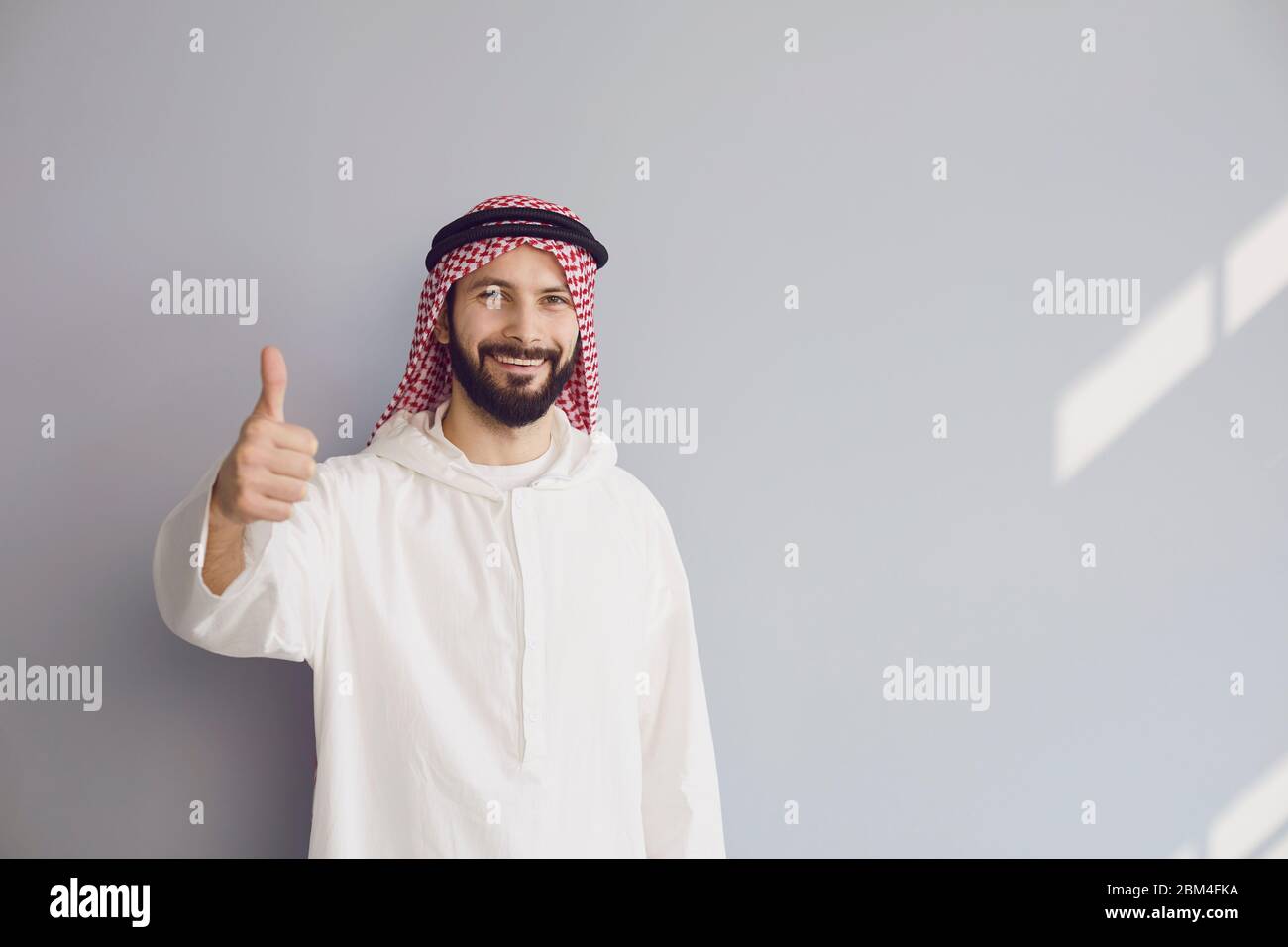 Attraente uomo arabo sorridente mostra pollice su sfondo grigio per il testo. Foto Stock