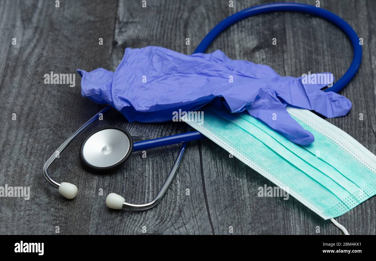 Un paio di guanti in gomma blu per uso medico, maschera chirurgica e stetoscopio blu su un tavolo di legno. Foto Stock