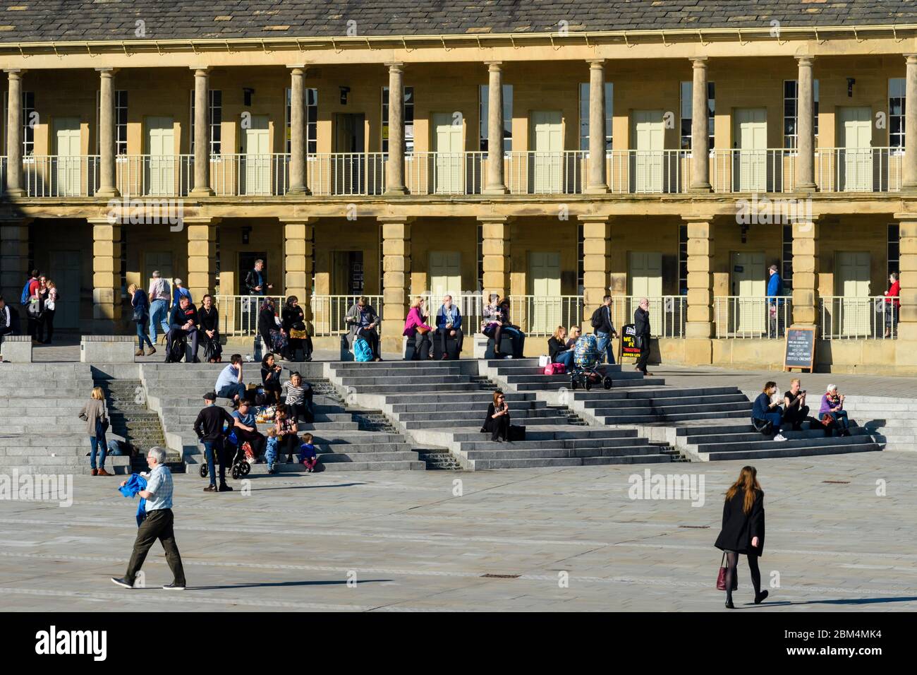 Cortile storico Piece Hall (piazza soleggiata, visitatori rilassanti, seduti su gradini e a piedi, archi colonnati) - Halifax, West Yorkshire, Inghilterra, Regno Unito. Foto Stock