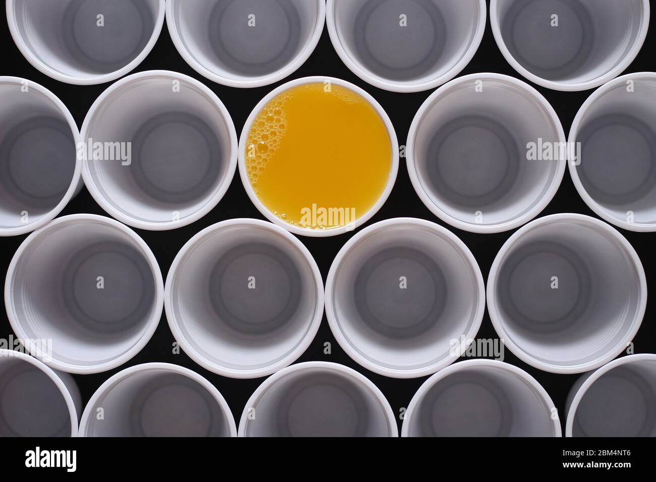 Succo d'arancia. Molte tazze monouso in plastica, una è riempita con succo d'arancia visto dall'alto. Foto Stock