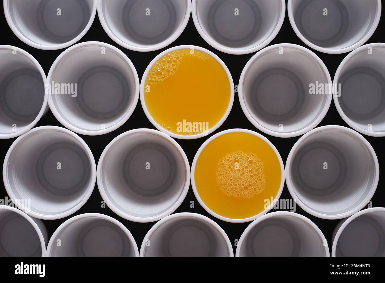 Molte tazze monouso in plastica, due sono riempite di succo d'arancia, visto dall'alto Foto Stock
