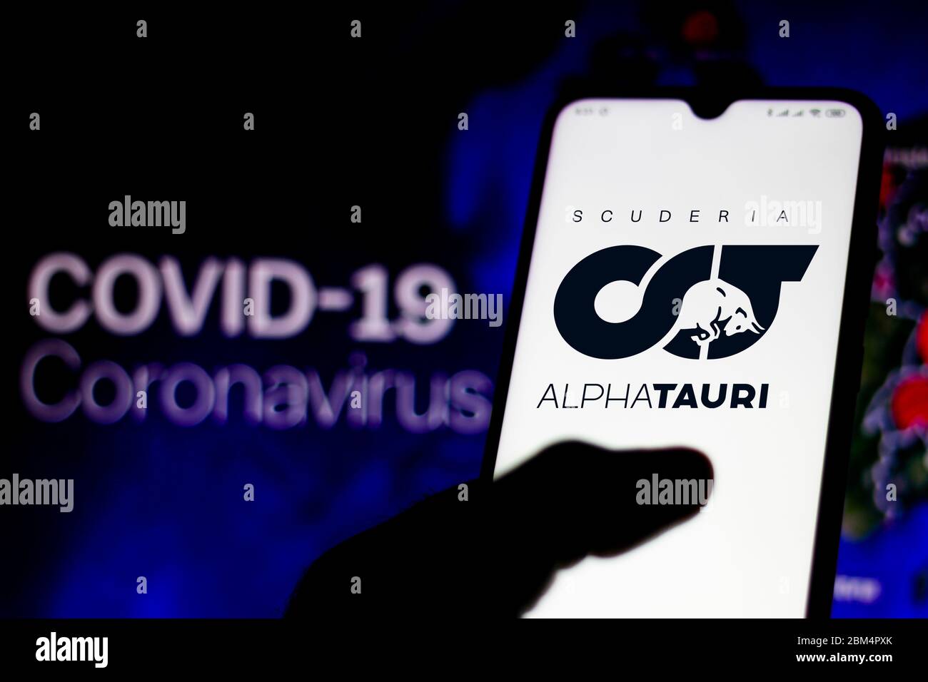 In questa illustrazione fotografica il logo della Scuderia AlphaTauri Honda è stato visualizzato su uno smartphone con una dicitura COVID-19 coronavirus come sfondo. Foto Stock