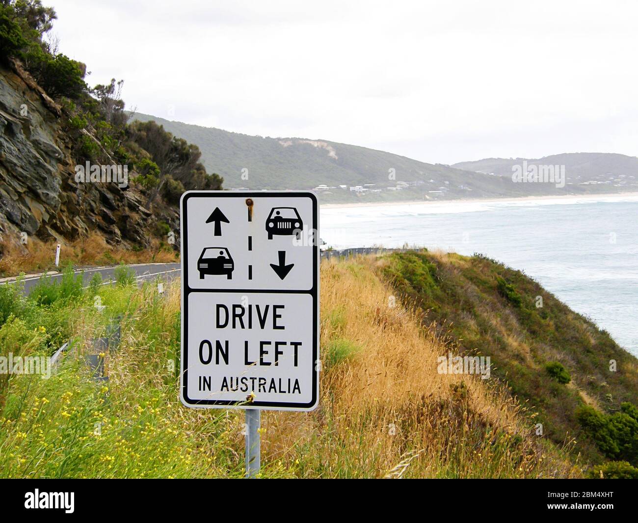 Cartello stradale australiano per ricordare ai conducenti di guidare sul lato sinistro della strada. Con oceano sullo sfondo. Foto Stock