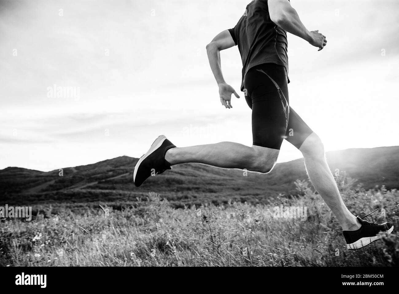 uomo runner correre su sentiero in montagna ai raggi del tramonto estivo Foto Stock