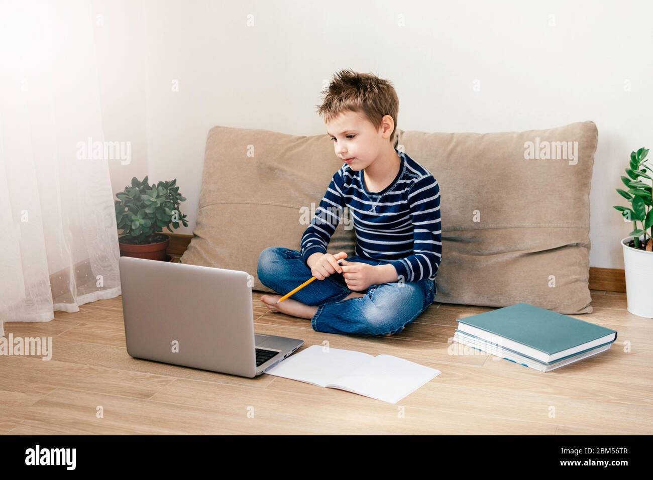 Giovane ragazzo che studia a casa utilizzando lezioni online sul laptop sul divano. Quarantena a casa. Formazione a distanza, formazione online per bambini. Foto Stock