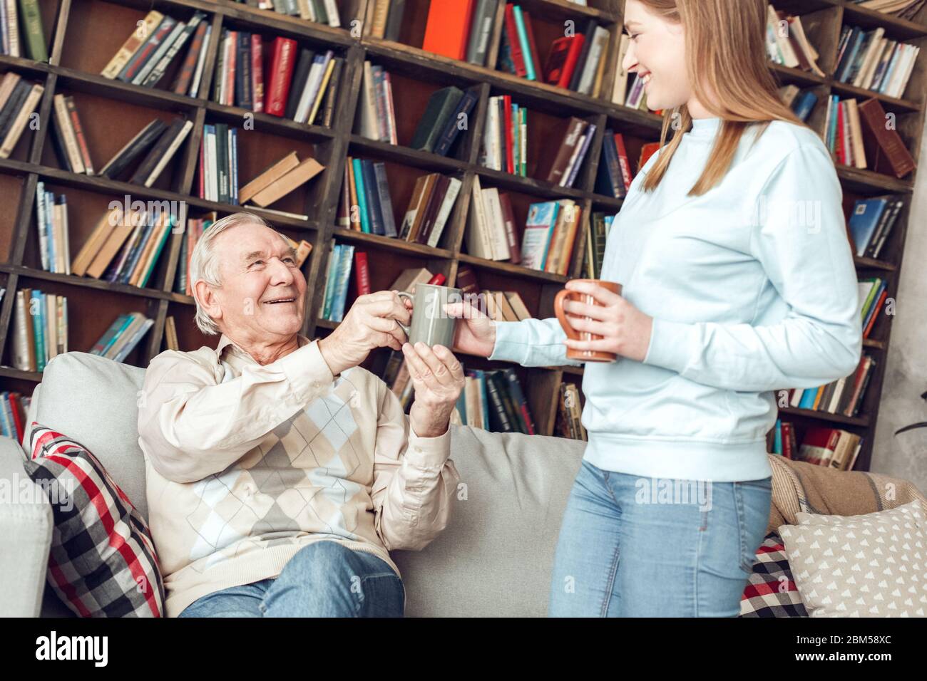 Padre e figlia a casa biblioteca donna che dà uomo tazza di caffè ridendo allegro Foto Stock