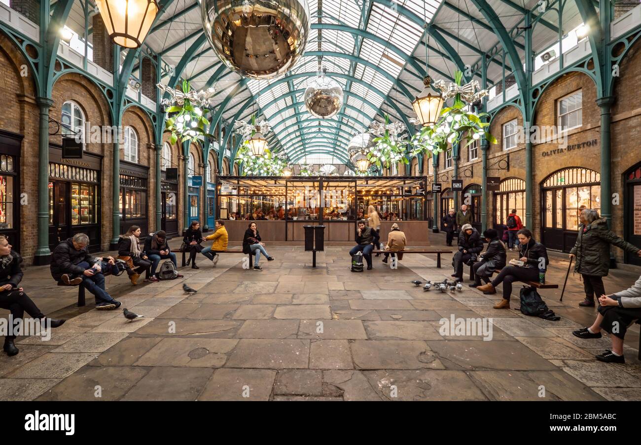 Covent Garden, Londra. Turisti e acquirenti riposano dal loro shopping natalizio in un'area con posti a sedere nel centro di Covent Garden di Londra. Foto Stock