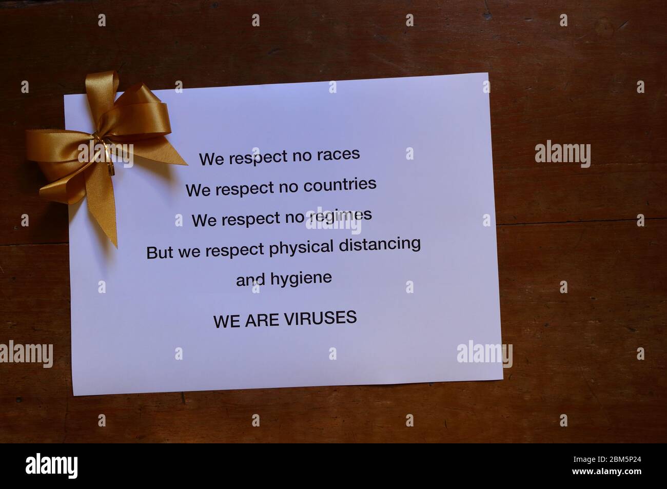 Segnale di avvertimento sul coronavirus stampato su carta bianca con arco di colore dorato posto sulla superficie di legno, concetto di distanza fisica Foto Stock
