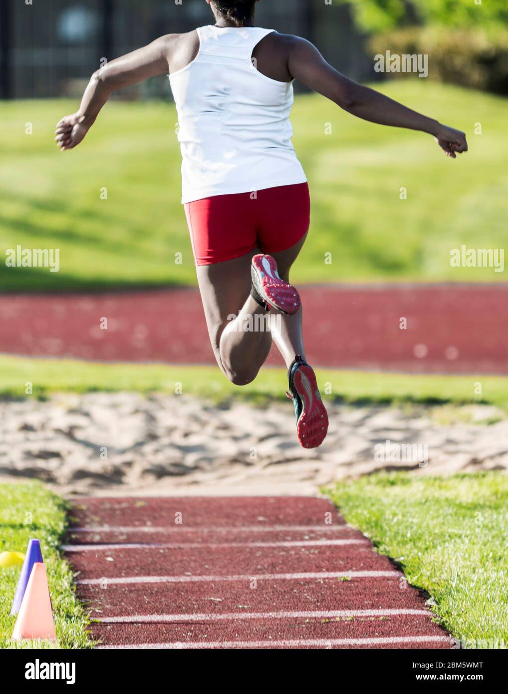 Una ragazza afro-americana della scuola superiore è nell'aria durante una concorrenza tripla di salto. Foto Stock