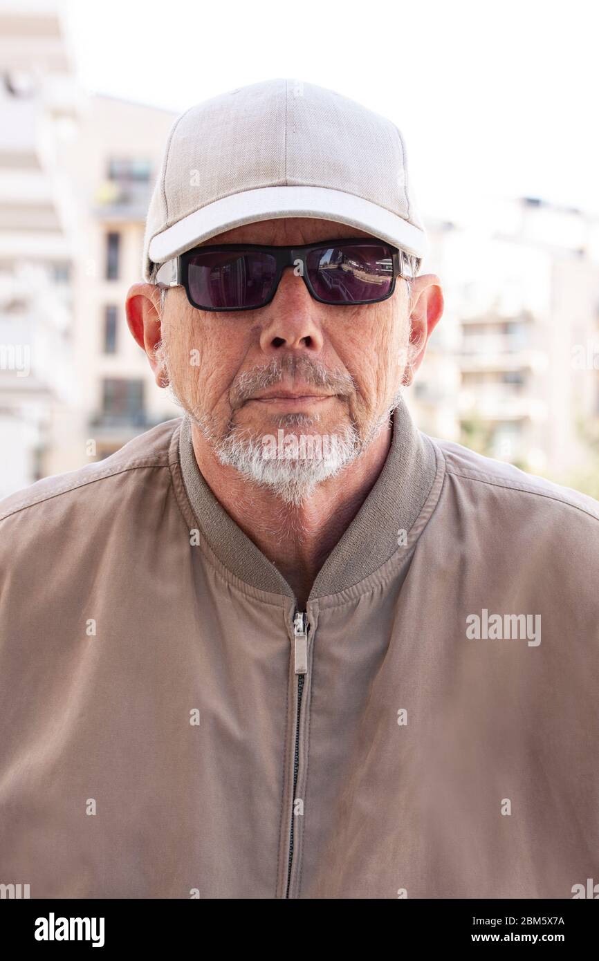 Uomo casual vestito di mezza età o anziano con occhiali da sole neri,  cappello bianco, indossare il windbreaker e una barba piccola grigia che  guarda direttamente nel camer Foto stock - Alamy