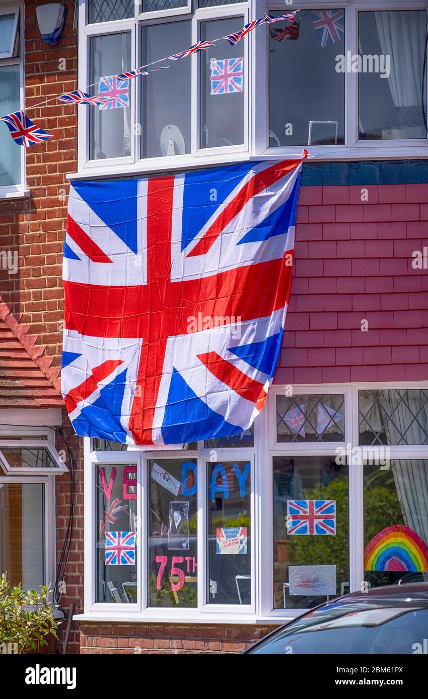Morden, Surrey, Regno Unito. 7 maggio 2020. La bandiera dell'Unione copre la facciata di una casa nel sud-ovest di Londra Borough di Merton per celebrare il 75 ° anniversario del VE Day, insieme con dipinto a mano grazie l'arcobaleno NHS. Credit: Malcolm Park/Alamy Live News. Foto Stock