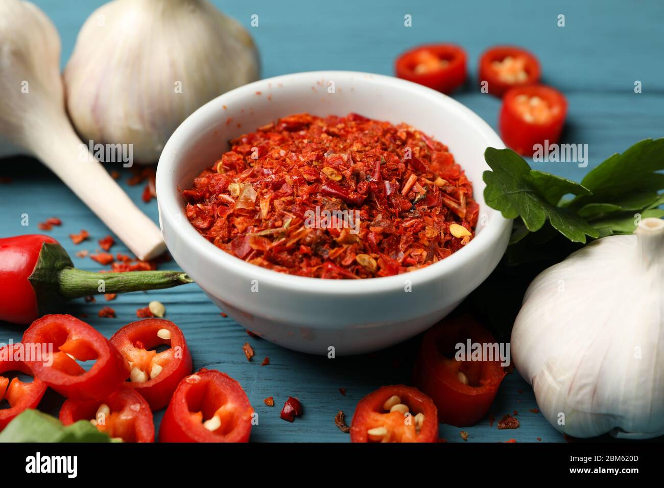 Ciotola con spezie a polvere calda e ingredienti su sfondo di legno Foto Stock