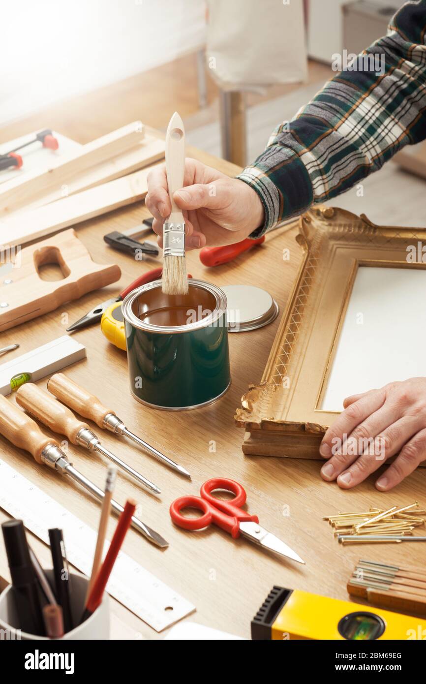 Arredatore verniciatura di un telaio in legno mani da vicino con gli strumenti per il fai da te, hobby e concetto di artigianato Foto Stock