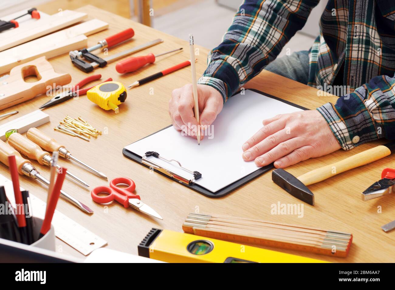 L'uomo delineando un progetto DIY su un blocco appunti con gli strumenti di lavoro tutto intorno, le mani vicino, hobby e concetto di artigianato Foto Stock