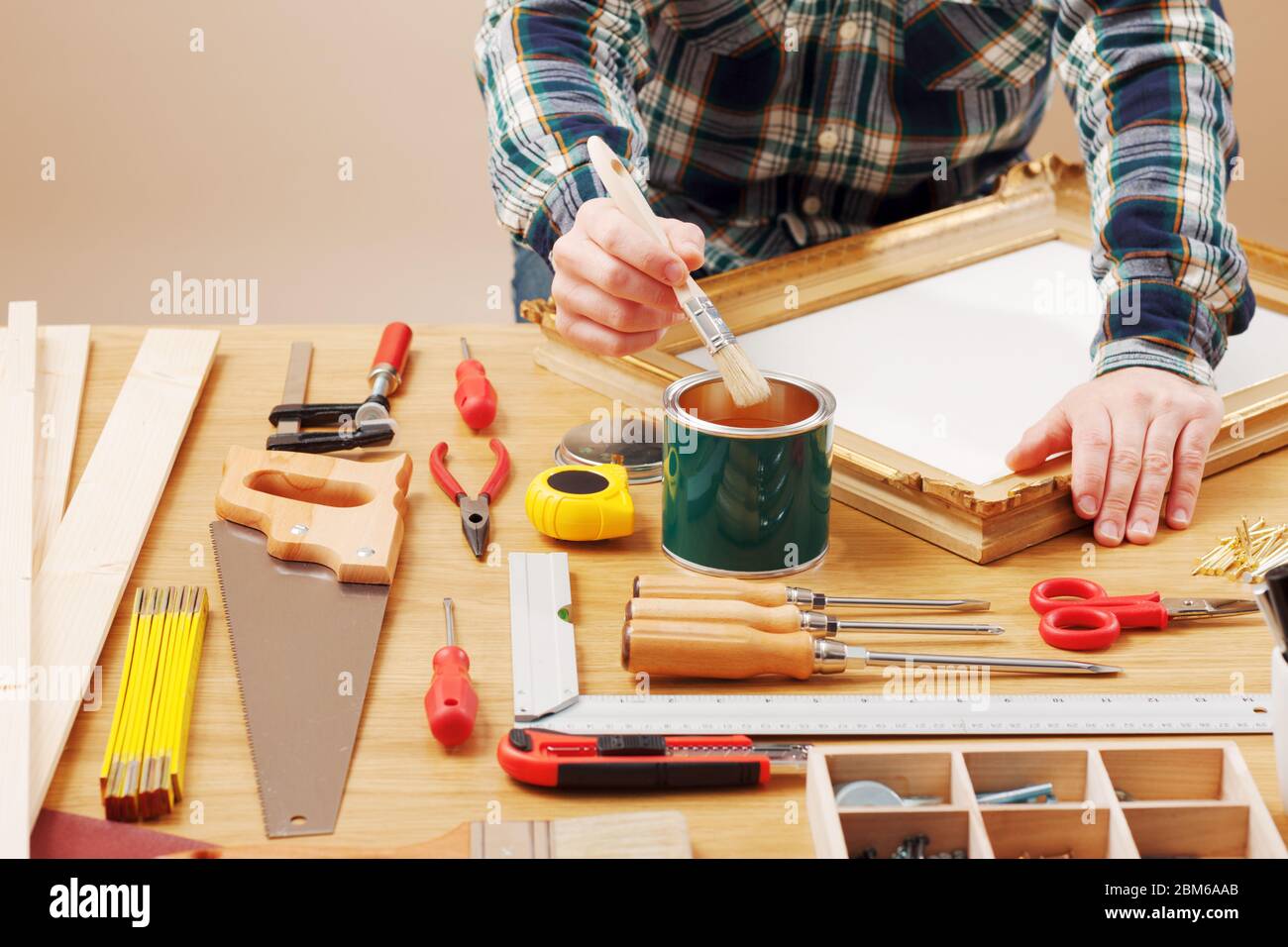 Arredatore verniciatura di un telaio in legno mani da vicino con gli strumenti per il fai da te, hobby e concetto di artigianato Foto Stock