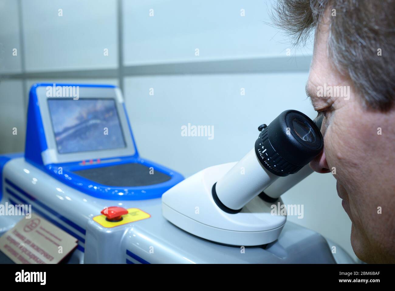 Tecnico maschio che guarda nell'oculare del dispositivo di microsaldatura laser ad alta precisione. Ottobre 08, 2019. Kiev, Ucraina Foto Stock