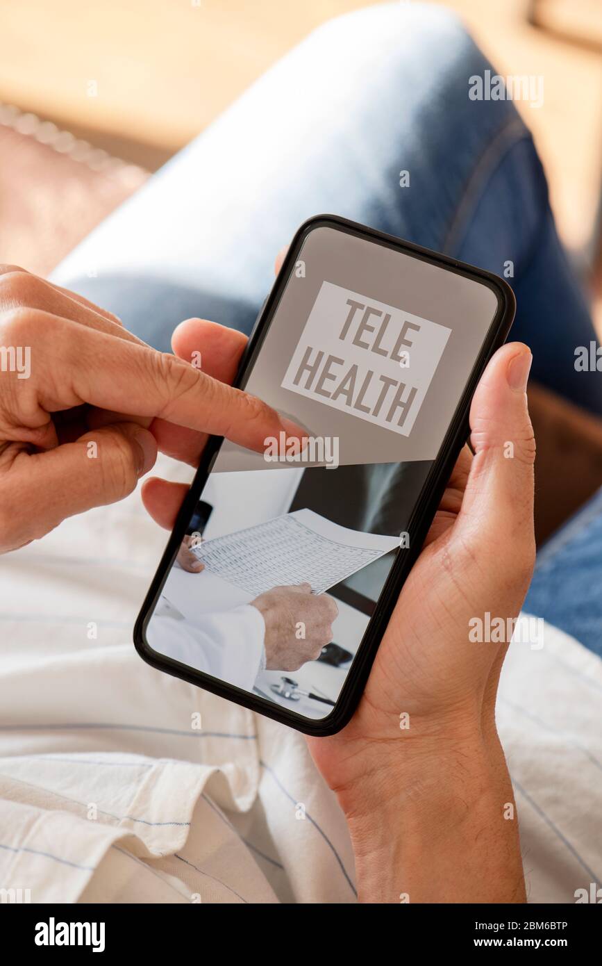 primo piano di un giovane caucasico, seduto comodamente in un divano, utilizzando il suo smartphone, con il testo di telesanità sul suo schermo Foto Stock