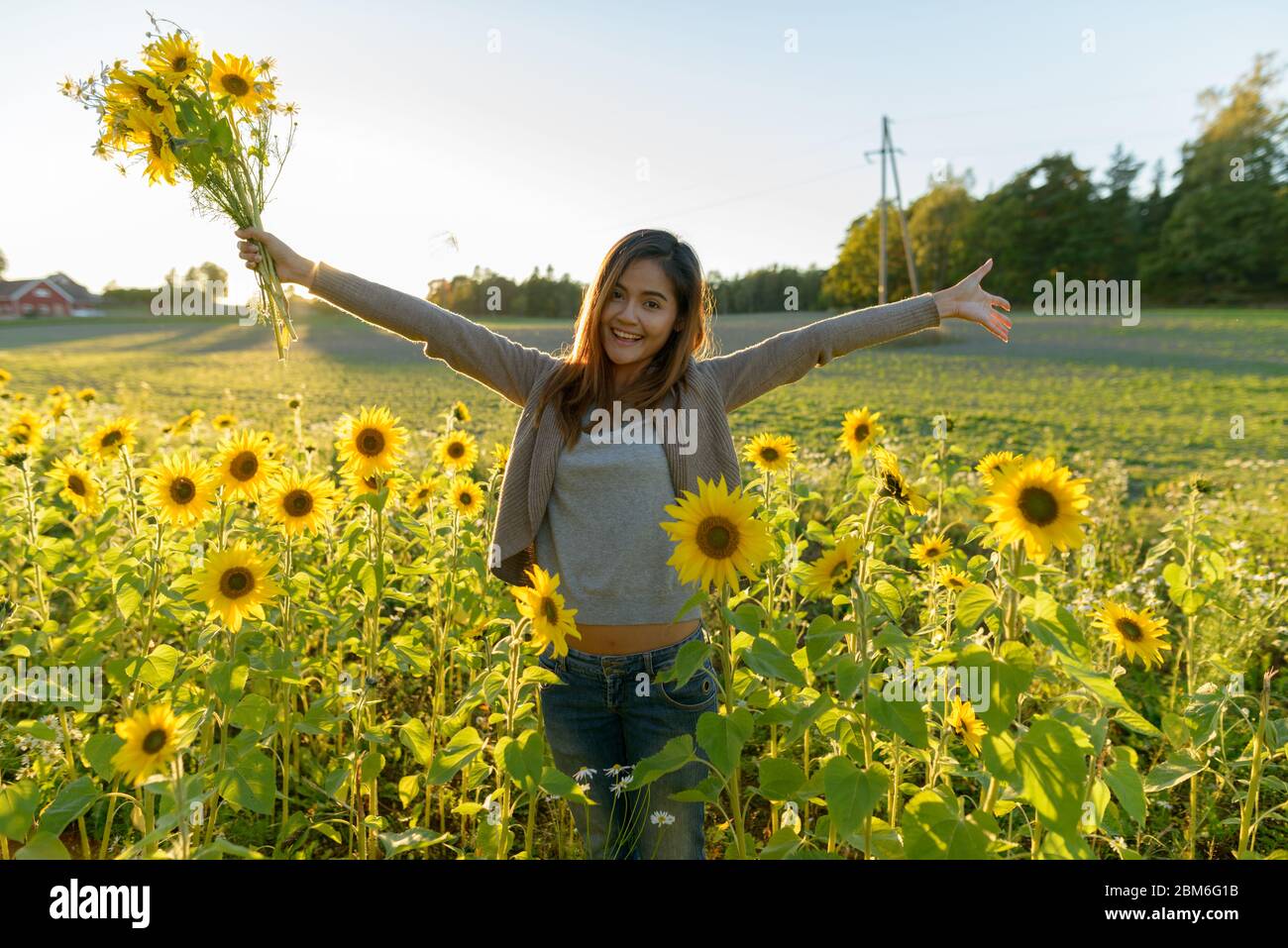 Felice giovane bella donna asiatica che tiene i fiori con le braccia aperte nella fattoria giardino di girasole Foto Stock