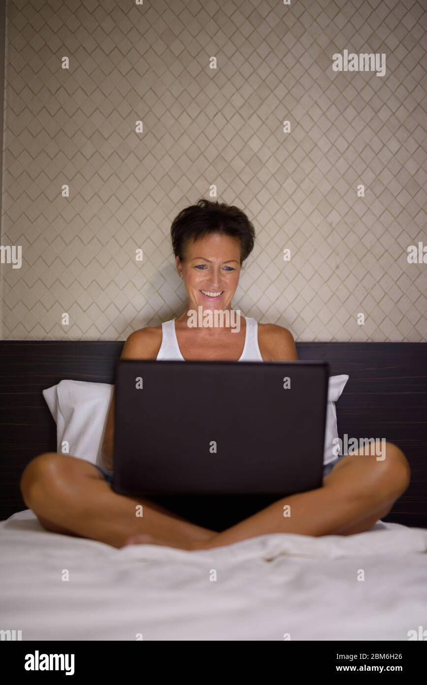 Felice donna matura bella turistica che usa il computer portatile in camera da letto Foto Stock