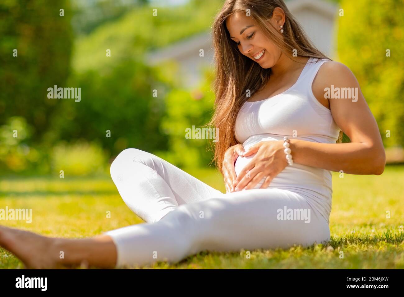 Donna incinta sorridente che forma un cuore sul ventre con le sue mani Foto Stock