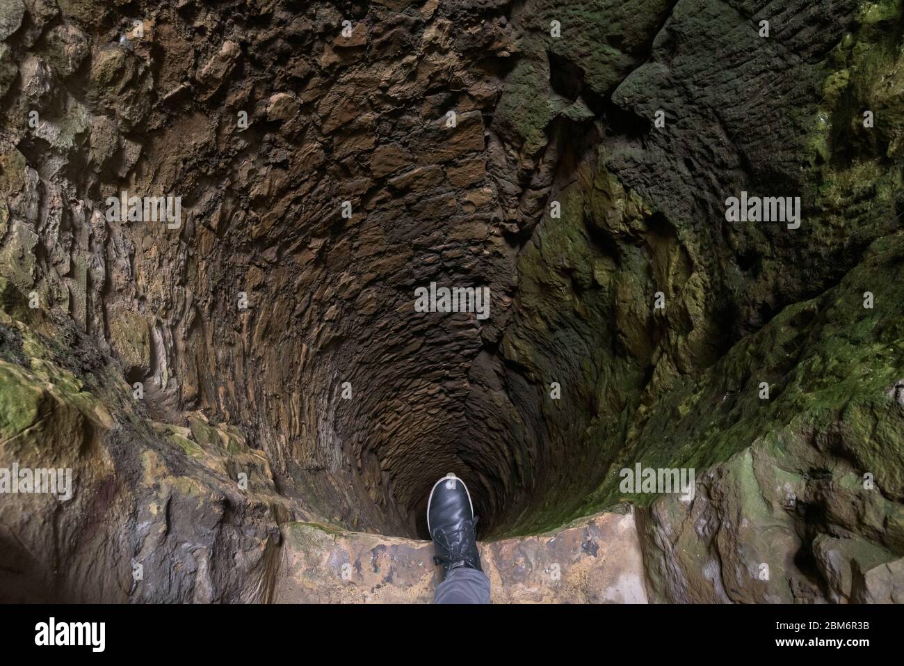 Persona in piedi con un piede sul bordo di un pericoloso profondo scuro bene fatto di pietra. Punti panoramici all'interno di Bock Casemates, Lussemburgo. Foto Stock