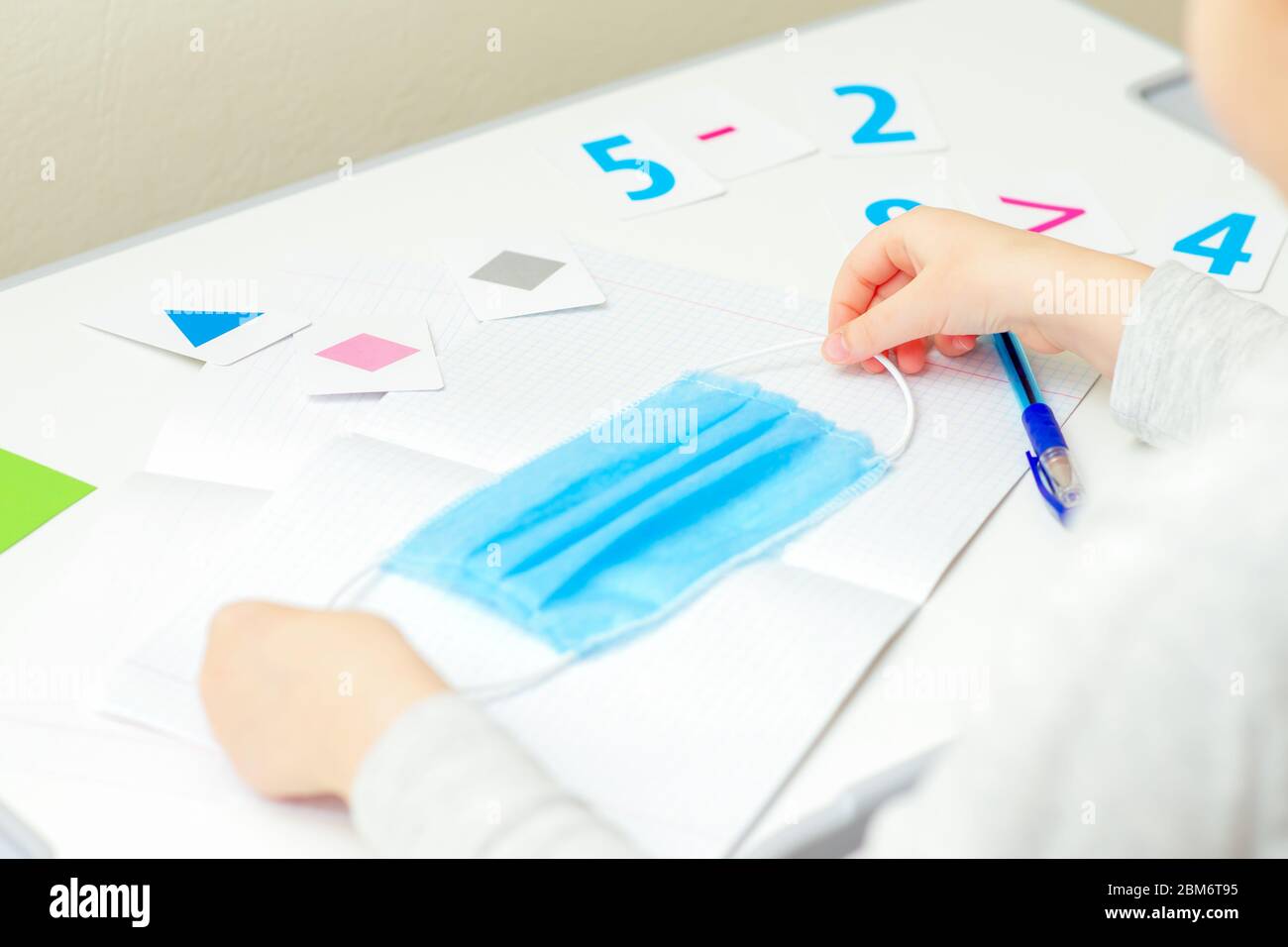 Mani per bambini che tengono una maschera protettiva medica sul notebook della scuola a casa. Concetto di apprendimento domestico. Foto Stock