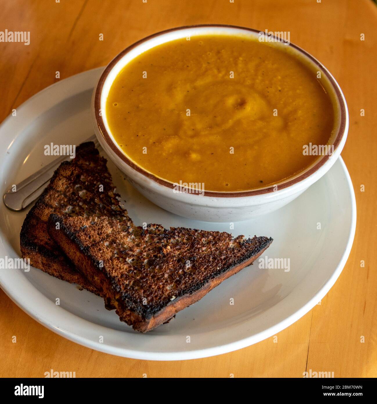 Zuppa di zucca in bianco ciotola di ceramica su tavolo di legno e due pezzi di toas visto formano un angolo - autunno piatto stagionale Foto Stock