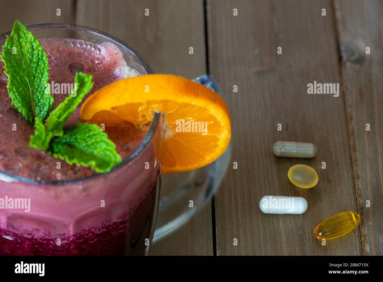 Bicchiere con succo di barbabietola rossa decorato con una fetta di foglie di limone e menta, su un tavolo di legno con integratori alimentari - concetto di scelte salutari Foto Stock