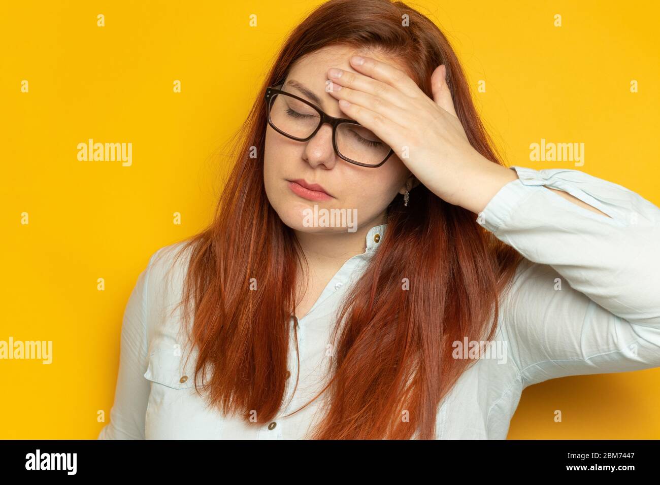 Giovane donna lavoratore in camicia e occhiali per la vista con mal di testa su sfondo giallo parete. Concetto di stress, fatica. Tenere le mani sulla testa Foto Stock