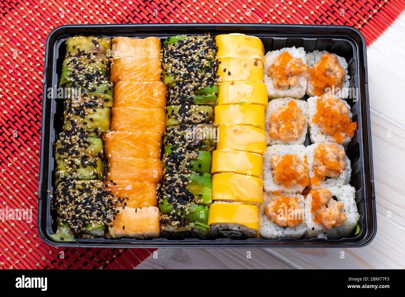 Set di panini sushi con salmone e verdure in vassoio nero su tappetino in vimini rosso. Un piatto giapponese di pesce Foto Stock