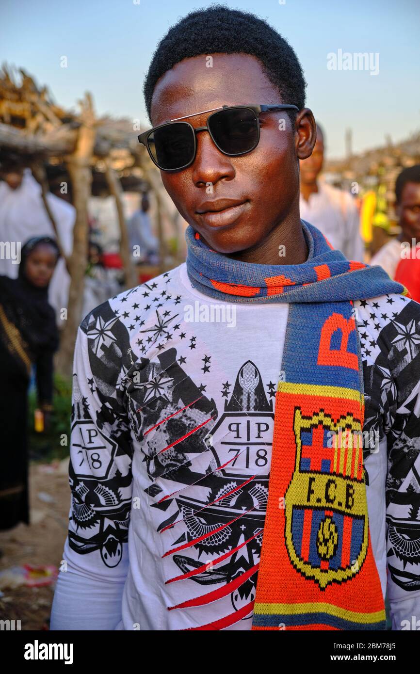 Giovane uomo con occhiali da sole e sciarpa barça nel mercato di Mahuta. Foto Stock