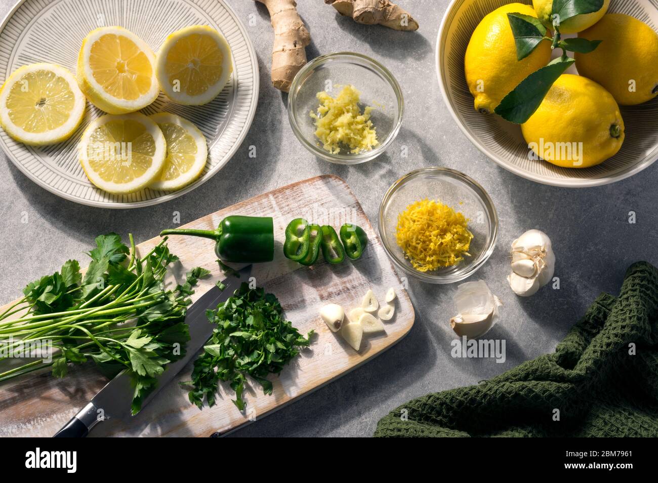 Ingredienti estivi, spezie e sapori freschi verdi e gialli. Prezzemolo, limone, aglio, peperoncino verde e zenzero. Scena rustica su un tavolo soleggiato. Altern Foto Stock