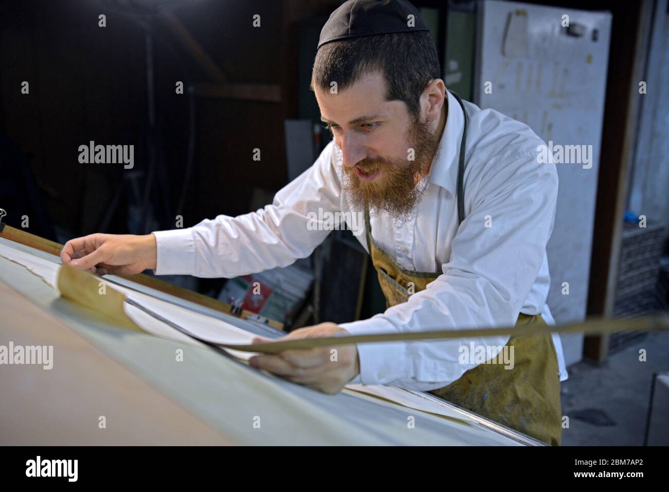 Un rabbino e maestro artigiano taglia un nuovo foglio di pergamena fatto nel suo seminterrato workshop.IT deve essere utilizzato per gli articoli religiosi. Foto Stock