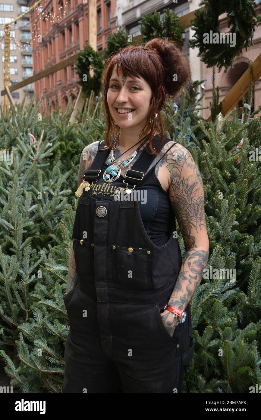 Una bella donna scozzese con tatuaggi che vendono alberi di Natale su Astor Place a Greenwich Village, Manhattan, New York City in un mite giorno di dicembre. Foto Stock