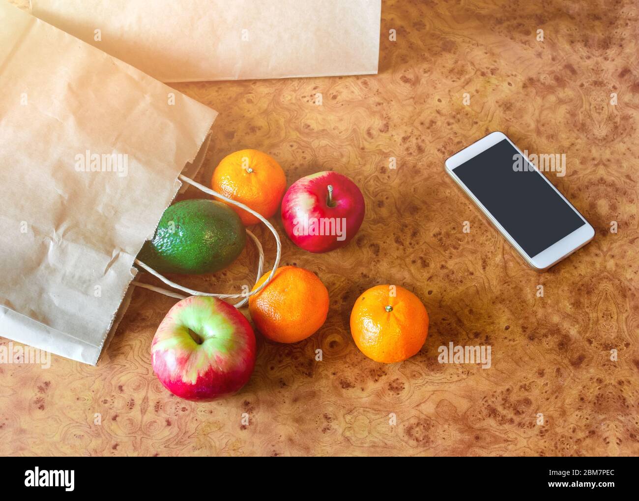 Sacchetti di carta, verdure fresche e frutta accanto al telefono cellulare sul tavolo da cucina. Acquisto online e consegna senza contatto. Foto Stock