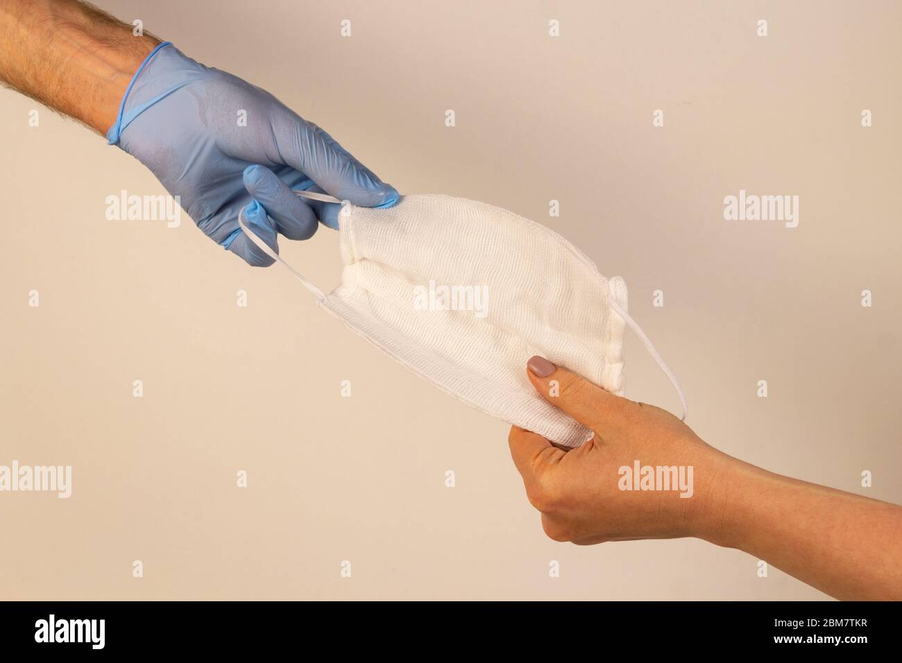 Una mano in un guanto blu dà ad una persona bisognosa una maschera medica. Primo piano isolato su sfondo bianco. Concetto di aiuto virale. Foto Stock