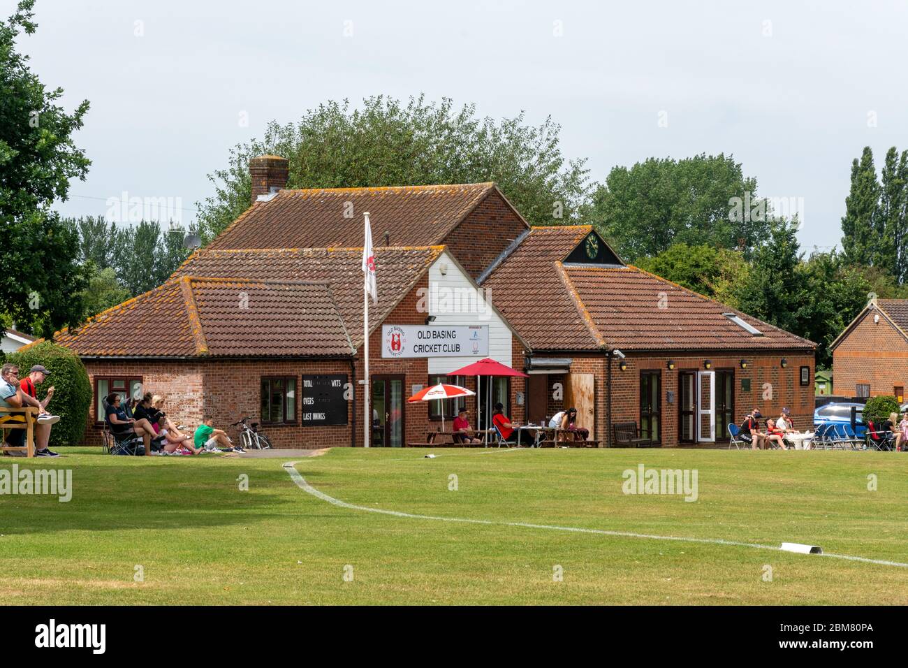 Persone che guardano un villaggio cricket partita fuori Old Basing Cricket Pavilion, Hampshire, UK Foto Stock